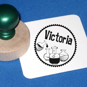 May include: A black and white rubber stamp with a circular design featuring the word "Victoria" and a graphic of four beakers. The beakers are filled with liquid and one beaker is pouring liquid into another beaker.