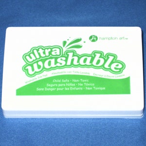 May include: A white rectangular ink pad with green text that reads "ultra washable" and "Child Safe - Non-Toxic". The ink pad is labeled "Washable Ink Pad" and has the brand name "hampton art" in green text.