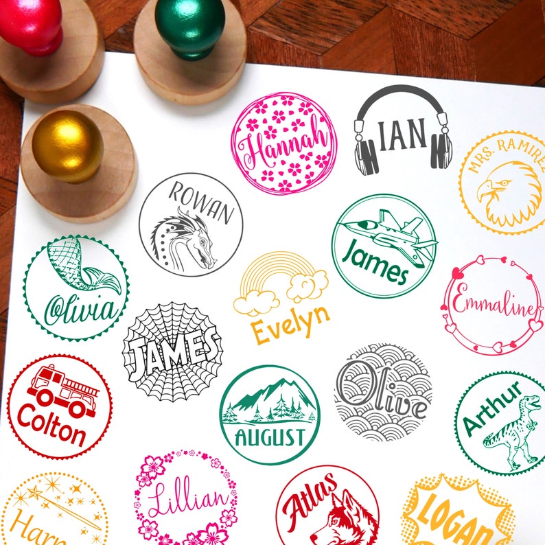 May include: A collection of 15 round personalised rubber stamps with various designs and names, including Olivia, Colton, Hannah, Rowan, James, Emmaline, James, Evelyn, Lillian, August, Olive, Atlas, Arthur, Logan, and Harry. The stamps are arranged on a white surface.