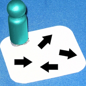 May include: A white card with four black arrows pointing in different directions. The card is sitting on a blue surface. A teal blue wooden peg is on top of the card.