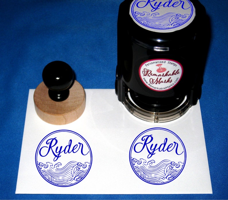 Puede incluir: Un sello de goma autoentintado con mango de madera. El sello presenta un dise&ntilde;o azul y blanco de olas y el nombre "Ryder" en letra cursiva. El sello est&aacute; hecho por "Remarkable Marks".