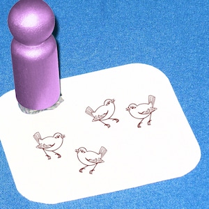 May include: A pink wooden stamp with a design of a small bird. The stamp is on a white surface with four impressions of the bird design.