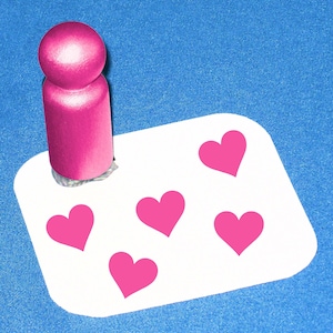 May include: A white card with five pink heart shapes. A pink heart-shaped stamp is on top of the card.