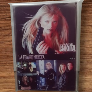 Könnte beinhalten: Eine DVD-Hülle von "La Femme Nikita" in einer transparenten Plastikhülle. Das Cover zeigt eine Frau mit einer Waffe, mit dem Titel und "Vol. 1".
