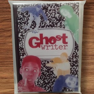 Könnte beinhalten: Ein Notizbuch mit einem schwarz-weiß gesprenkelten Einband, auf dem in Rot die Worte "Ghost Writer" stehen. Der Einband zeigt Bilder von Menschen in verschiedenen Posen. Das Notizbuch ist in einer transparenten Plastiktüte versiegelt.