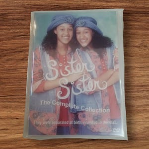 Op de afbeelding: Een dvd van de tv-serie "Sister, Sister: The Complete Collection". De cover toont een foto van de twee hoofdrolspeelsters met spijkergoedhoeden en -vesten. De tekst op de cover luidt "Sister, Sister" en "The Complete Collection."