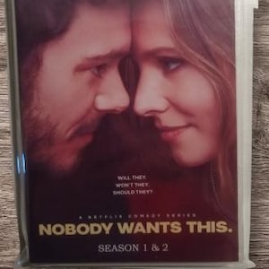 May include: A DVD case for the Netflix comedy series "Nobody Wants This," starring Kristen Bell and Adam Brody. The cover art shows the actors' faces close together. The DVD is sealed in plastic, with the text "Season 1 & 2" visible.