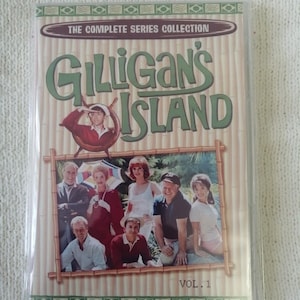 以下が含まれることがあります： 「ギルigan's Island: The Complete Series Collection, Vol. 1」のDVDセット。カバーには、番組タイトルが緑色で表示され、キャストの写真と竹スタイルのボーダーが描かれています。 DVDは透明なプラスチックケースに入っています。
