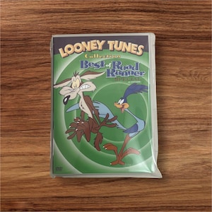 Könnte beinhalten: Eine DVD-Hülle mit der Looney Tunes Collection: Best of Road Runner Special. Das Cover zeigt Wile E. Coyote und den Road Runner vor einem grünen Hintergrund. Die DVD ist in Plastik versiegelt.