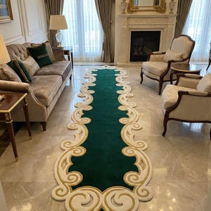 May include: A long, ornate green and cream-colored runner rug with a scrolling design. The rug is placed on a marble floor in a living room setting, with a sofa, chairs, and fireplace visible in the background.