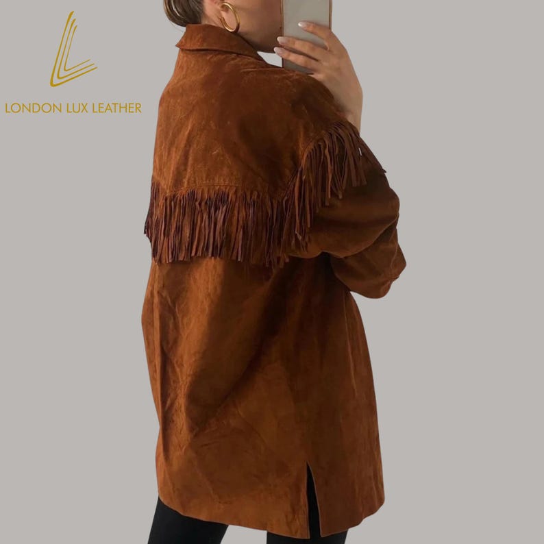 May include: A brown suede jacket with fringe detailing across the upper back. The jacket has a collared neckline and a long, relaxed fit. The brand logo "LONDON LUX LEATHER" is visible on the upper left.