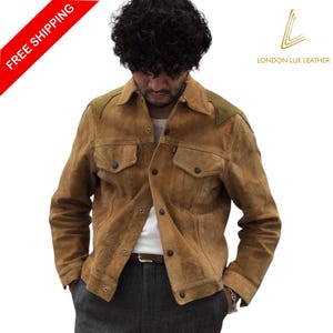 May include: A brown suede jacket with olive green shoulder accents. The jacket has two chest pockets and a button-up front. The model is wearing a white shirt and gray pants. The jacket is from London Lux Leather.