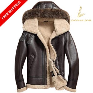 May include: A dark brown leather jacket with a fur-lined hood and a beige shearling interior. The jacket has a zipper closure, pockets, and buckle details. The London Lux Leather logo is visible.