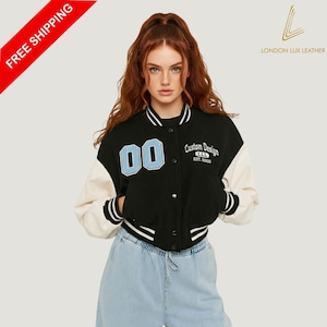 May include: A black varsity jacket with cream-colored sleeves. The jacket features the number "00" in light blue on the chest and the words "Custom Design" in white. The jacket has a button-up front and a striped collar and cuffs.