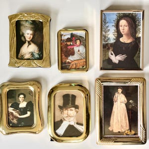 May include: Collection of six antique gold-toned picture frames, each containing a different portrait. The frames vary in shape and design, with ornate detailing. The portraits depict figures in historical attire, showcasing a variety of artistic styles.
