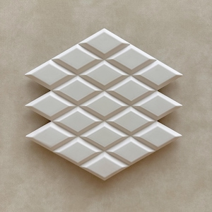May include: Three white diamond-shaped tiles arranged in a stack. Each tile features a raised, repeating diamond pattern. The tiles are set against a neutral, textured background, creating a clean, modern aesthetic. Ideal for home decor.