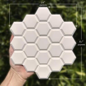May include: A white, honeycomb-shaped decorative tile, measuring 7.5 inches by 8.1 inches. The tile features a three-dimensional design with multiple hexagonal cells. The background is a blurred green, suggesting an outdoor setting.