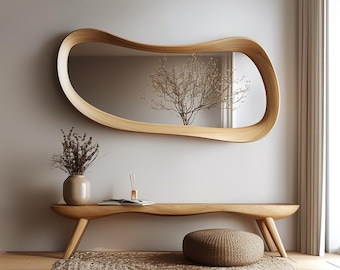 May include: A modern interior scene featuring a large, organically shaped wooden mirror above a matching wooden bench. The bench has a curved design and is supported by angled legs. A woven rug and a round ottoman complete the space.