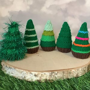 Peut inclure: Une collection de cinq petits arbres de Noël faits à la main. Les arbres sont de différentes nuances de vert, certains avec des éléments décoratifs comme des rayures et des guirlandes. Ils sont présentés sur une tranche de bois, sur fond de ciel nuageux et d'herbe verte.