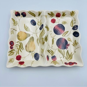 May include: A rectangular, off-white ceramic serving platter with a wavy edge. The platter is divided into two sections and decorated with a painted design of pears, plums, pomegranates, and leaves in shades of red, purple, green, and yellow.