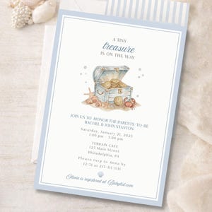 May include: Baby shower invitation with a watercolor illustration of a treasure chest, seashells, and a crab. The invitation has a light blue border and includes event details: date, time, and location.