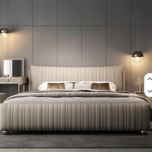 May include: A beige upholstered bed with a vertically ribbed headboard and footboard. The bed has gold-colored accents on the legs and frame. Two gold-colored spherical pendant lights hang above the bed, illuminating the room.
