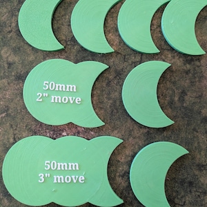 K&ouml;nnte beinhalten: Hellgr&uuml;ne, halbmondf&ouml;rmige Spielsteine. Zwei Teile tragen die Aufschrift "50mm 2" move" und "50mm 3" move". Die Teile sind auf einer strukturierten Oberfl&auml;che angeordnet.