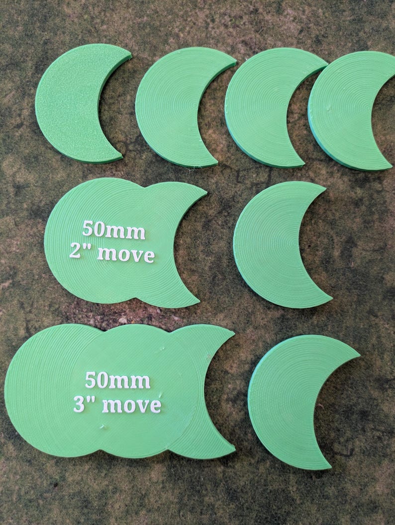 K&ouml;nnte beinhalten: Hellgr&uuml;ne, halbmondf&ouml;rmige Spielsteine. Zwei Teile tragen die Aufschrift "50mm 2" move" und "50mm 3" move". Die Teile sind auf einer strukturierten Oberfl&auml;che angeordnet.