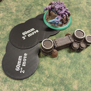 K&ouml;nnte beinhalten: Miniatur-Tabletop-Spielteile auf einer gr&uuml;nen Oberfl&auml;che. Eine lila Kreaturenfigur auf einer gr&uuml;nen Basis, ein Holzkarren mit F&auml;ssern und schwarze Bewegungsmarker mit den Texten "60mm" und "3" move" und "2" move".
