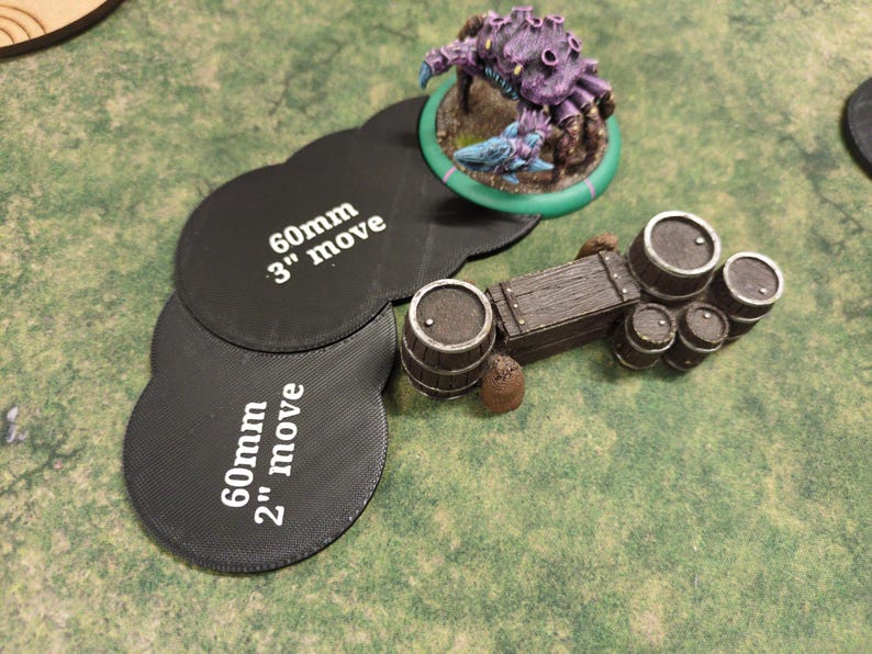 K&ouml;nnte beinhalten: Miniatur-Tabletop-Spielteile auf einer gr&uuml;nen Oberfl&auml;che. Eine lila Kreaturenfigur auf einer gr&uuml;nen Basis, ein Holzkarren mit F&auml;ssern und schwarze Bewegungsmarker mit den Texten "60mm" und "3" move" und "2" move".