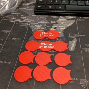 K&ouml;nnte beinhalten: Rote Spielmarken mit einem Tab, angeordnet auf einer Weltkarte. Zwei Marken tragen die Aufschrift "25mm 2" move" und "25mm 3" move". Im Hintergrund ist eine schwarze Tastatur zu sehen. Die Marken haben einen Durchmesser von ca. 2,5 cm.