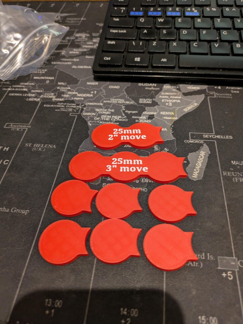 K&ouml;nnte beinhalten: Rote Spielmarken mit einem Tab, angeordnet auf einer Weltkarte. Zwei Marken tragen die Aufschrift "25mm 2" move" und "25mm 3" move". Im Hintergrund ist eine schwarze Tastatur zu sehen. Die Marken haben einen Durchmesser von ca. 2,5 cm.