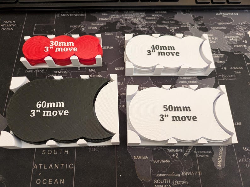 K&ouml;nnte beinhalten: Vier Spielbewegungs-Tabletts in Wei&szlig;, Rot und Schwarz. Jedes Tablett enth&auml;lt kreisf&ouml;rmige Token mit dem Text "3" move" und den Ma&szlig;en 30 mm, 40 mm, 50 mm und 60 mm.