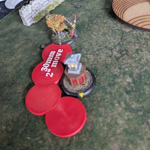 Puede incluir: Una escena de juego de mesa con una figura en miniatura, una linterna y marcadores circulares rojos. Los marcadores están etiquetados con "30mm 2" move". La escena está ambientada en una superficie verde texturizada. La figura tiene una lanza.