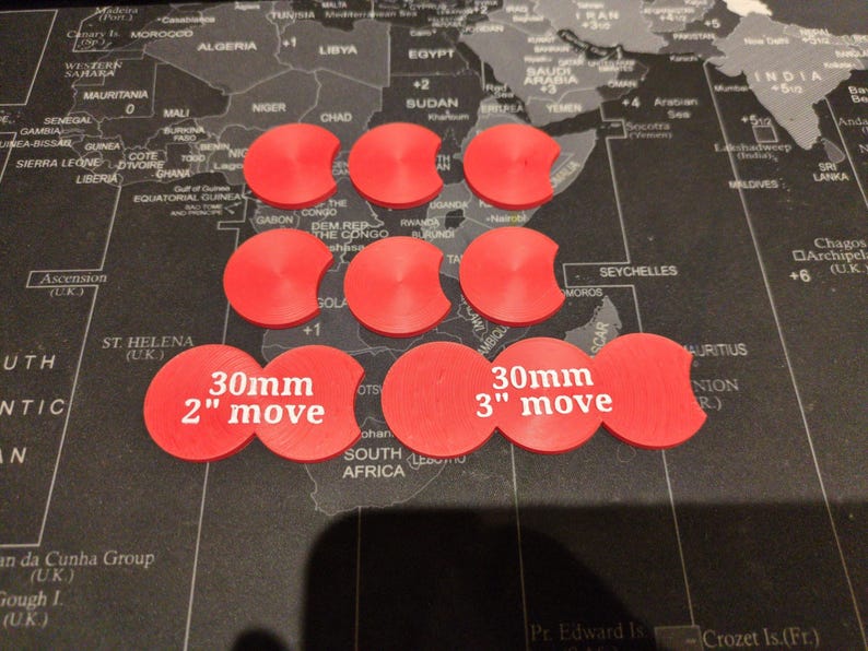 K&ouml;nnte beinhalten: Neun rote Spielmarken mit gebogenem Rand sind auf einer Weltkarte angeordnet. Zwei Marken sind mit "30mm 2" move" und "30mm 3" move" beschriftet. Die Marken werden wahrscheinlich f&uuml;r Brett- oder Strategiespiele verwendet.