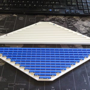 May include: Two white and blue geometric shaped objects. The top object is white with horizontal grooves. The bottom object is white with blue rectangular pieces. A black keyboard is in the background.