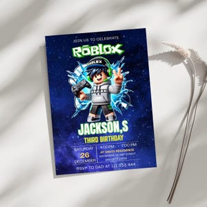 May include: A rectangular birthday invitation card featuring a dark blue space background with the Roblox logo at the top. A cartoon character wearing a grey hoodie and green headphones holds a game controller. Text includes JACKSON,S THIRD BIRTHDAY.