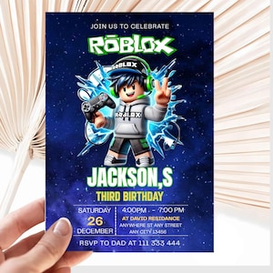 May include: A rectangular birthday invitation card featuring a Roblox theme with a dark blue starry background. A cartoon character wearing a grey hoodie and green headphones holds a game controller. Text includes JOIN US TO CELEBRATE, ROBLOX, JACKSON,S THIRD BIRTHDAY, and event details.