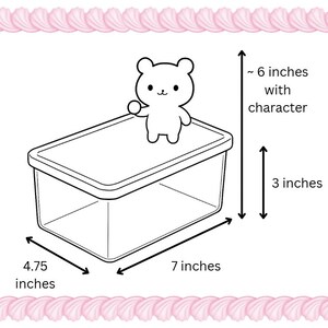 Puede incluir: Un recipiente de pl&aacute;stico transparente con tapa, coronado por un personaje de oso de dibujos animados. El recipiente mide aproximadamente 17,78 cm de largo, 12,07 cm de ancho y 7,62 cm de alto. El personaje a&ntilde;ade unos 15,24 cm a la altura. La imagen est&aacute; enmarcada con un borde rosa.