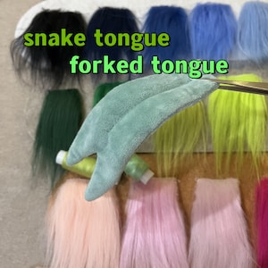 May include: A light green, forked tongue made of soft fabric is held by scissors, with the text "snake tongue forked tongue" in green. Various colours of faux fur are in the background, including black, blue, green, yellow, pink, and purple.