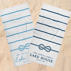May include: Two white beach towels with blue nautical rope designs and horizontal stripes. One towel reads "The Taylor Lake" and the other reads "The Howel Family Lake House Caddo Lake".