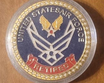 May include: A commemorative coin with a clear plastic case. The coin features the words "UNITED STATES AIR FORCE" around the edge, with a central emblem and the word "RETIRED" in red. The coin has gold, blue, and silver tones.