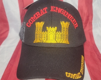 May include: Black baseball cap with "COMBAT ENGINEER" embroidered in red and gold. The cap features a gold castle emblem and additional text on the side. The background is an American flag.