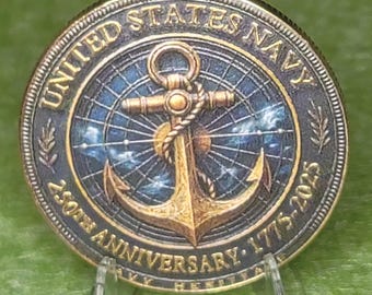 May include: A circular United States Navy challenge coin featuring a central gold-toned anchor wrapped in rope against a blue celestial map background. The border text reads UNITED STATES NAVY and 250TH ANNIVERSARY 1775-2025 with small leaf icons.