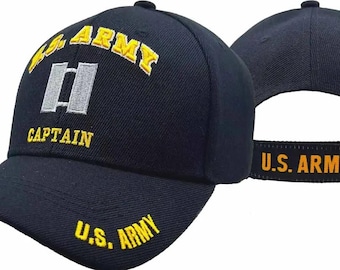May include: A navy blue baseball cap featuring embroidered yellow text that reads U.S. ARMY and CAPTAIN. The front displays a silver and grey captain rank insignia. The brim also features yellow U.S. ARMY text, and the back strap reads U.S. ARMY.