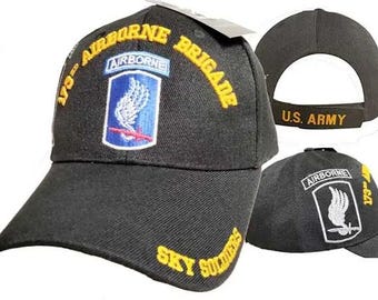 May include: A black baseball cap featuring the embroidered text 173rd AIRBORNE BRIGADE in yellow, a blue and white Airborne patch with a wing and sword emblem, and the yellow text SKY SOLDIERS on the brim. The back strap displays U.S. ARMY in yellow.