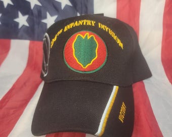 May include: Black baseball cap featuring the emblem of the 24th Infantry Division. The cap has a curved brim and the word "VICTORY" embroidered on the side. The cap is set against the backdrop of an American flag.