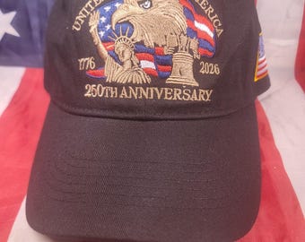 May include: Black baseball cap with embroidered design. The design includes an eagle, the Statue of Liberty, and the text "UNITED STATES OF AMERICA 1776 2026 250TH ANNIVERSARY". The cap has a curved brim.