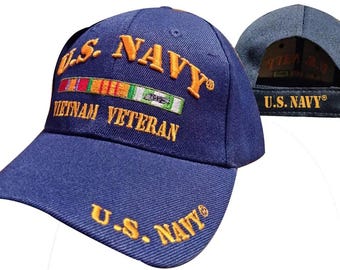 May include: A navy blue baseball cap featuring embroidered yellow text that reads U.S. NAVY and VIETNAM VETERAN. The front displays a colorful ribbon bar, and the brim includes additional U.S. NAVY text. The back strap also features U.S. NAVY.