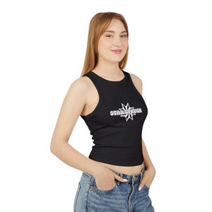 May include: A black ribbed tank top featuring a white graphic design on the chest. The graphic consists of a stylised star shape with the text "STARSTRUCK" written in a bold, rounded font across the centre of the star. The top has a crew neckline.